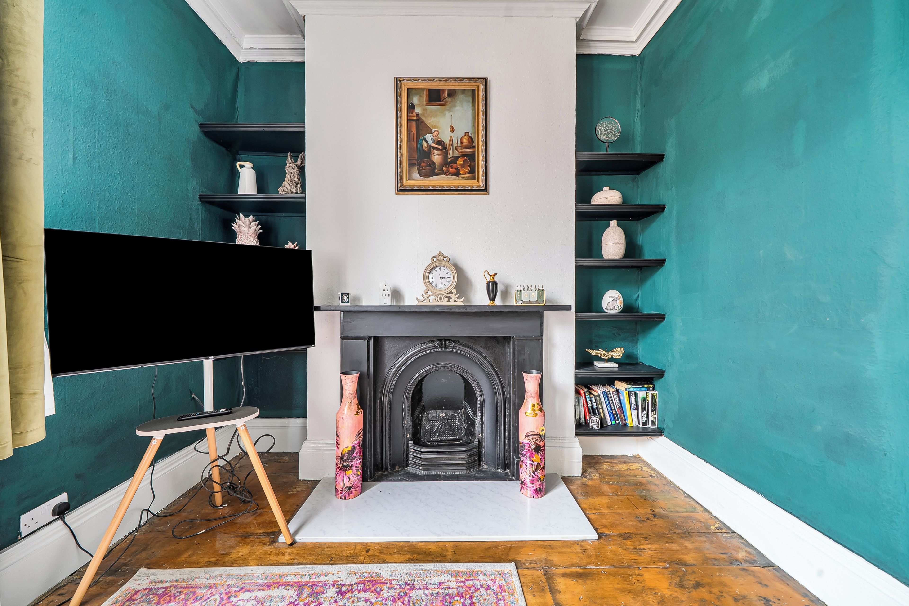 A room with teal walls, a fireplace, a mounted television, and a bookshelf.