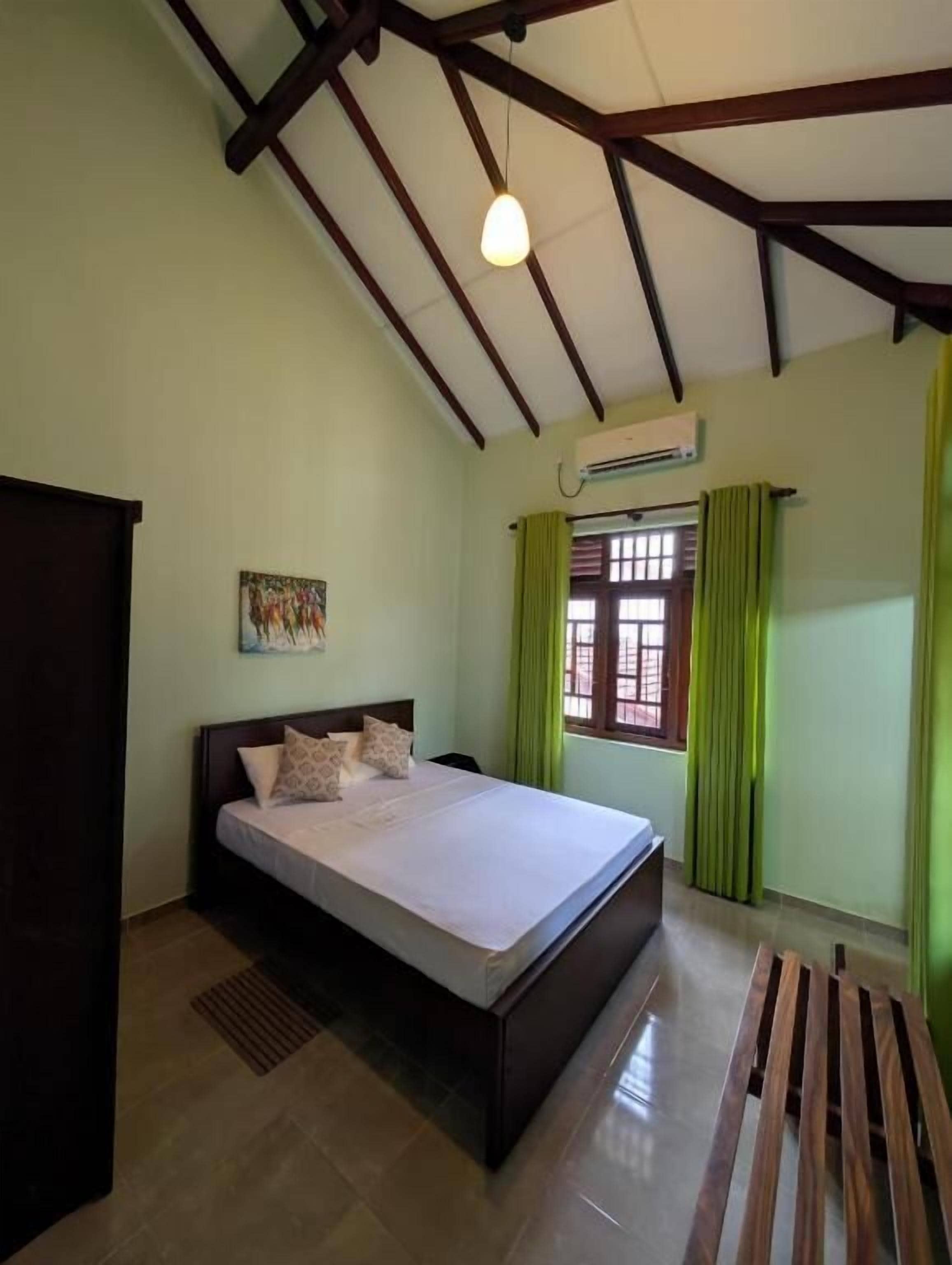 Un dormitorio con una cama, un banco de madera, una ventana con cortinas y un ventilador de techo.