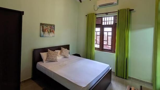 Un dormitorio con una cama, un banco de madera, una ventana con cortinas y un ventilador de techo.