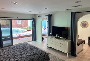 Une chambre avec un lit, une télévision, une commode et une vue sur une piscine et un espace extérieur.