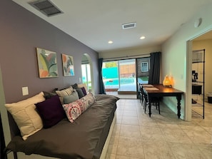 A modern living room with a sofa, a dining table, and a view of the outside. - Private Pool House | Walk to 5 Points Dining & Shops (Jacksonville)