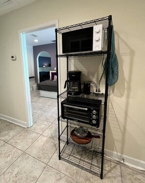 Un coin cuisine avec un présentoir en métal noir sur lequel sont posés une machine à café, un four grille-pain et un bol.