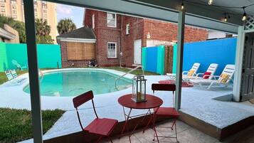 A covered outdoor area with a pool, red chairs, and a table.