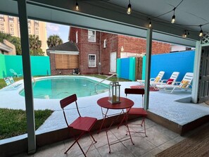 A covered outdoor area with a pool, red chairs, and a table.