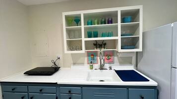A kitchen with a white countertop, a sink, and a built-in shelf with colorful glassware.