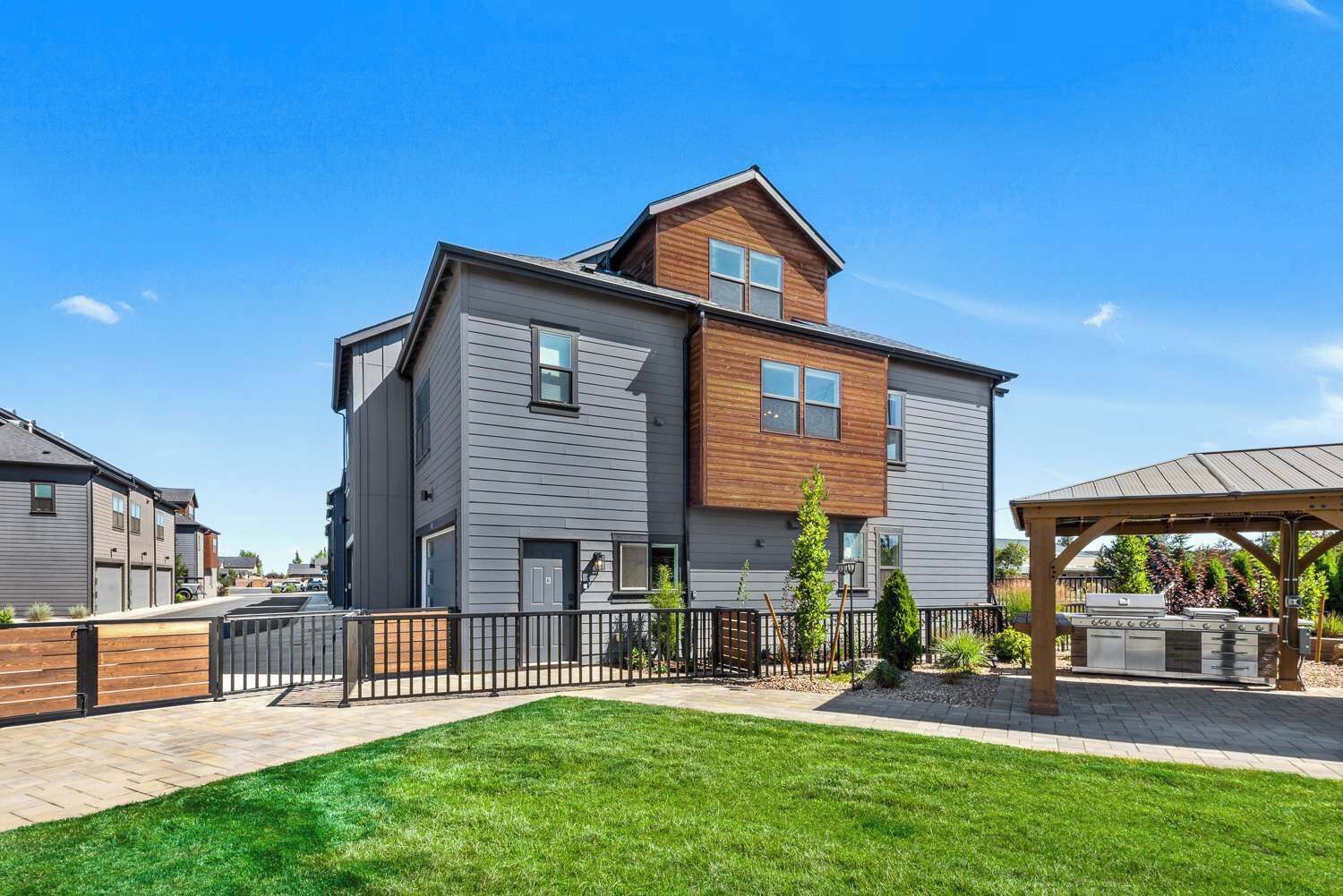 A two-story residential building with a modern design, a covered outdoor grill area, and a well-maintained lawn.
