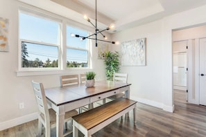 A dining area with a wooden table, chairs, and a bench. There are windows with a view of trees and a ceiling light fixture. - Dual Unit Townhouse in the heart of Bend (Bend)