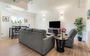 A modern living room with a sofa, armchair, and a dining area with a table and chairs.