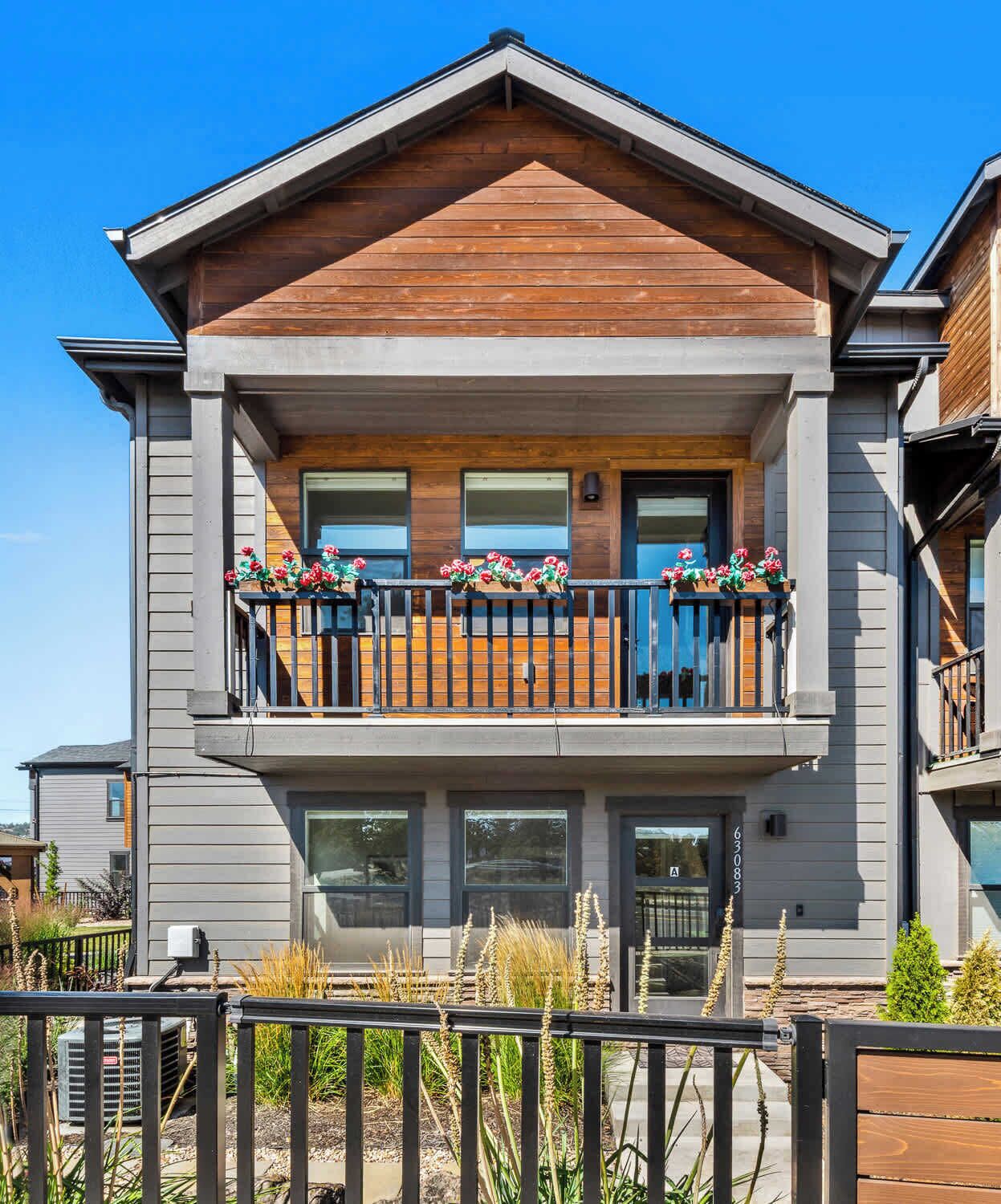Ein zweistöckiges Haus mit Balkon, großen Fenstern und einer Holzfassade.