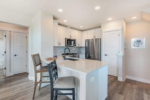 A modern kitchen with white cabinetry, stainless steel appliances, and a central island with bar stools. - Dual Unit Townhouse in the heart of Bend (Bend)