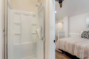 A modern bedroom with a glass shower enclosure, a bed with a striped bedspread, and a wooden ceiling fan. - Dual Unit Townhouse in the heart of Bend (Bend)