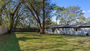 A residential property with a grassy yard, a wooden fence, and a white house with a dark roof. - San Pablo Retreat Near Mayo Clinic Mins to Beaches (Jacksonville)
