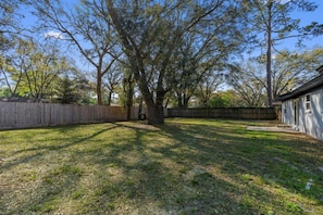 A backyard with a wooden fence, a tree, and a building. - 10 Min to Mayo & Beach • Sleeps 5 • Clean & Quiet (Jacksonville)