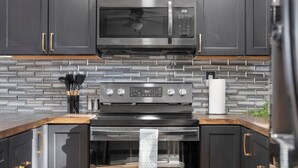 A kitchen with dark cabinetry, a stainless steel microwave, a stove, and a tiled backsplash. - San Pablo Retreat Near Mayo Clinic Mins to Beaches (Jacksonville)