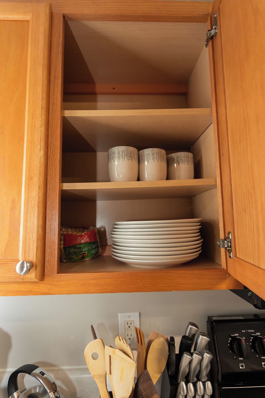 Un mueble de madera con estantes que contiene tazas de cerámica, platos y un paquete de pasta.
