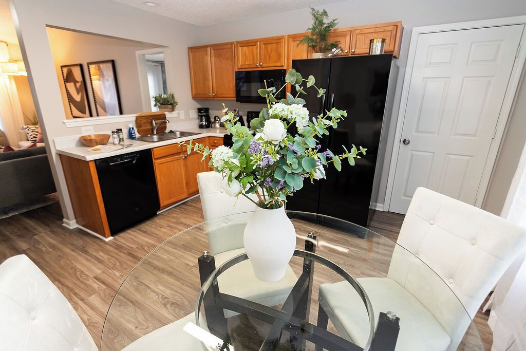 A modern kitchen with wooden cabinets, a black refrigerator, and a dining area with a glass table and white chairs.