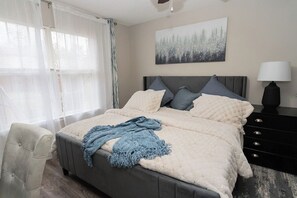 Ein Schlafzimmer mit einem Bett, einem Nachttisch, einer Lampe, einem Sessel und einem Bild an der Wand.