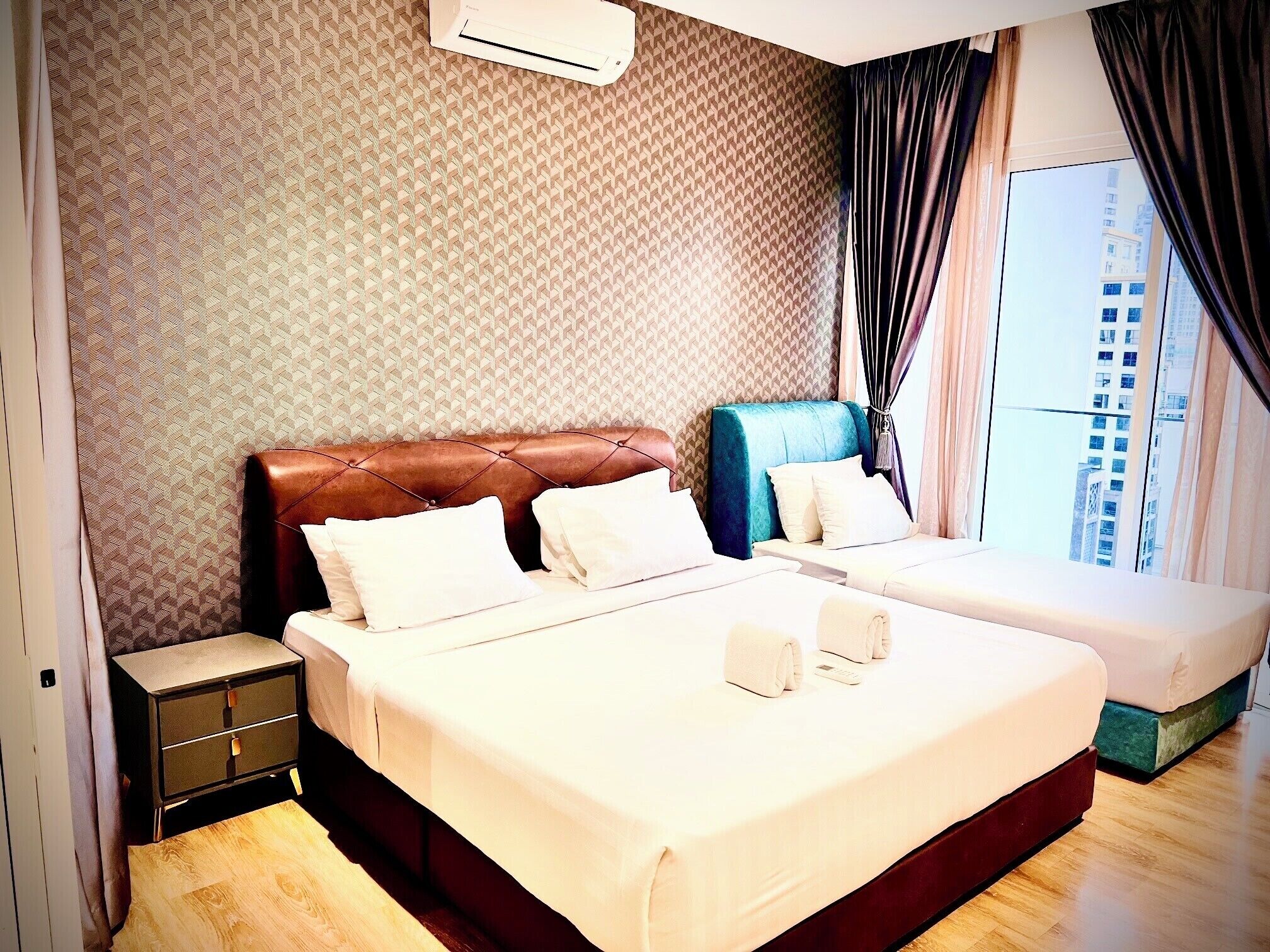 A hotel room with a large bed, a smaller bed, a nightstand, and a window with curtains.