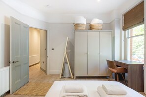 A bedroom with a bed, a desk, a wardrobe, and a window with a view. - GuestReady - Charming London Retreat for Four (London)