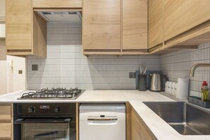 A modern kitchen with a gas stove, oven, dishwasher, stainless steel sink, and wooden cabinets. - GuestReady - Charming London Retreat for Four (London)