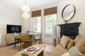 A living room with a television, a fireplace, a sofa, and a dining area with chairs. - GuestReady - Charming London Retreat for Four (London)