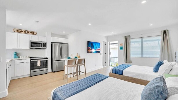 A modern hotel room with two beds, a kitchenette, a dining area, and a balcony with a city view. - Kemp`s Ridley 6 - Oceanfront Studio - Heated Pool (Lauderdale-by-the-Sea)