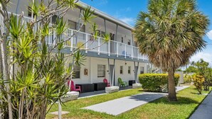 A two-story building with a balcony, outdoor seating, and a palm tree. - Kemp`s Ridley 6 - Oceanfront Studio - Heated Pool (Lauderdale-by-the-Sea)