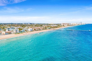 Paisatge costaner amb una platja, aigües blaves cristal·lines i un moll que s'endinsxa a la mar.