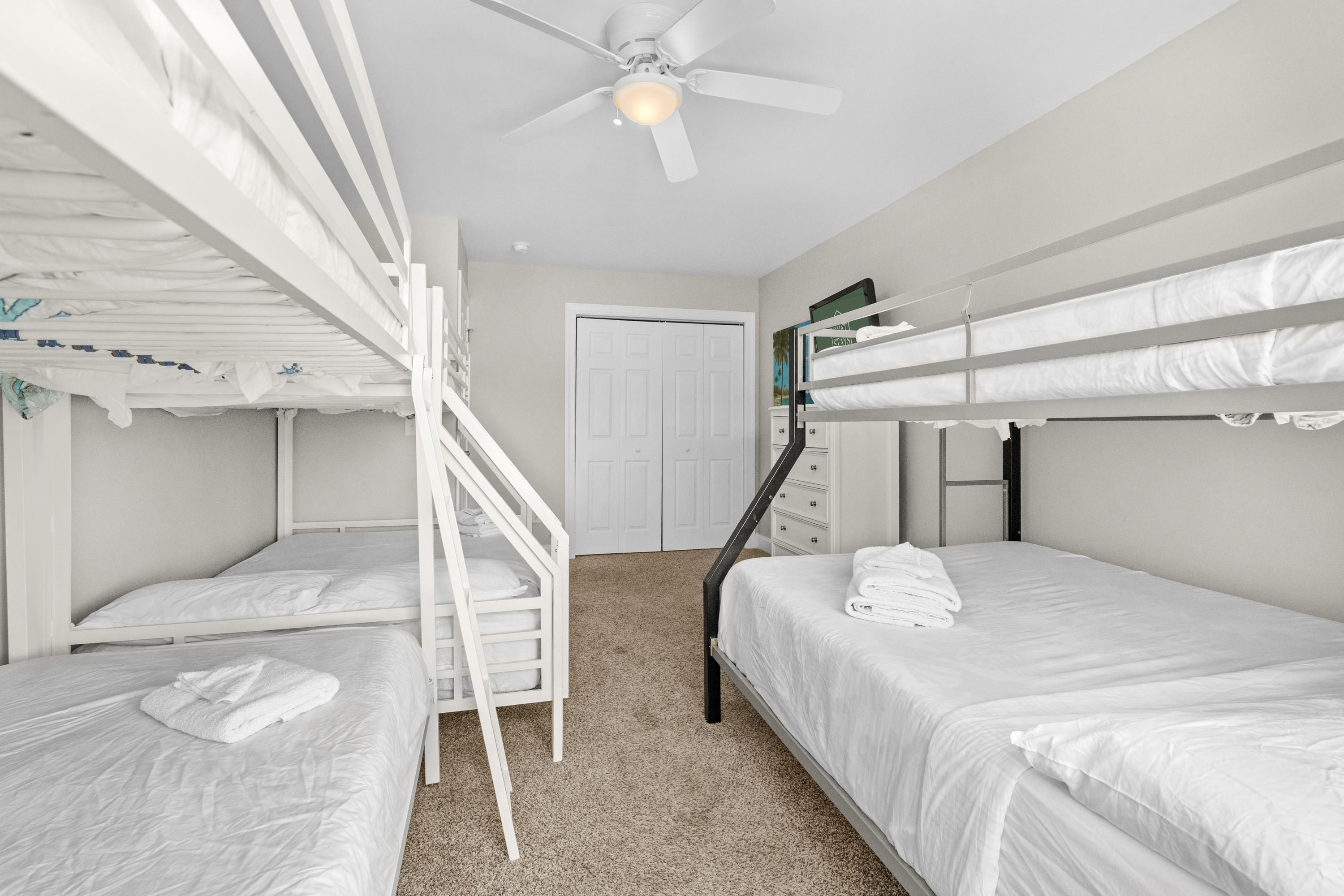 A room with bunk beds, a ceiling fan, a door, and a small dresser.