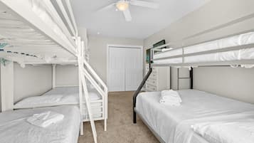 A room with bunk beds, a ceiling fan, a door, and a small dresser.