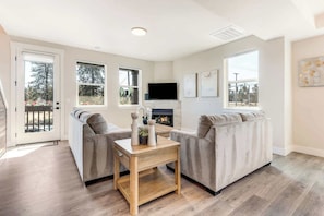 Ein Wohnzimmer mit zwei Sofas, einem Couchtisch, einem Kamin und großen Fenstern.