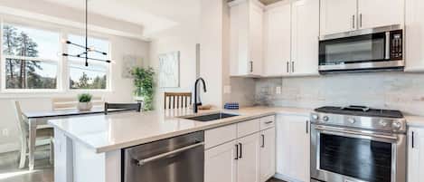 A modern kitchen with white cabinetry, stainless steel appliances, and a central island with a dishwasher.