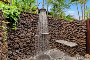 Eine Steinsäule mit Wasserspiel, darunter ein Wasserfall und eine Sitzgelegenheit.