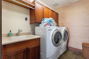 A laundry area with a washing machine, a sink, and wooden cabinets. - Pakui Street Estate by Gather - Hualalai Golf Estate w/ Private Pool & Spa (Kailua Kona)
