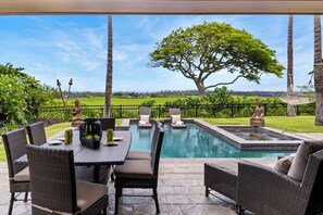 An outdoor pool area with wicker furniture and statues, surrounded by a fence and greenery. - Pakui Street Estate by Gather - Hualalai Golf Estate w/ Private Pool & Spa (Kailua Kona)