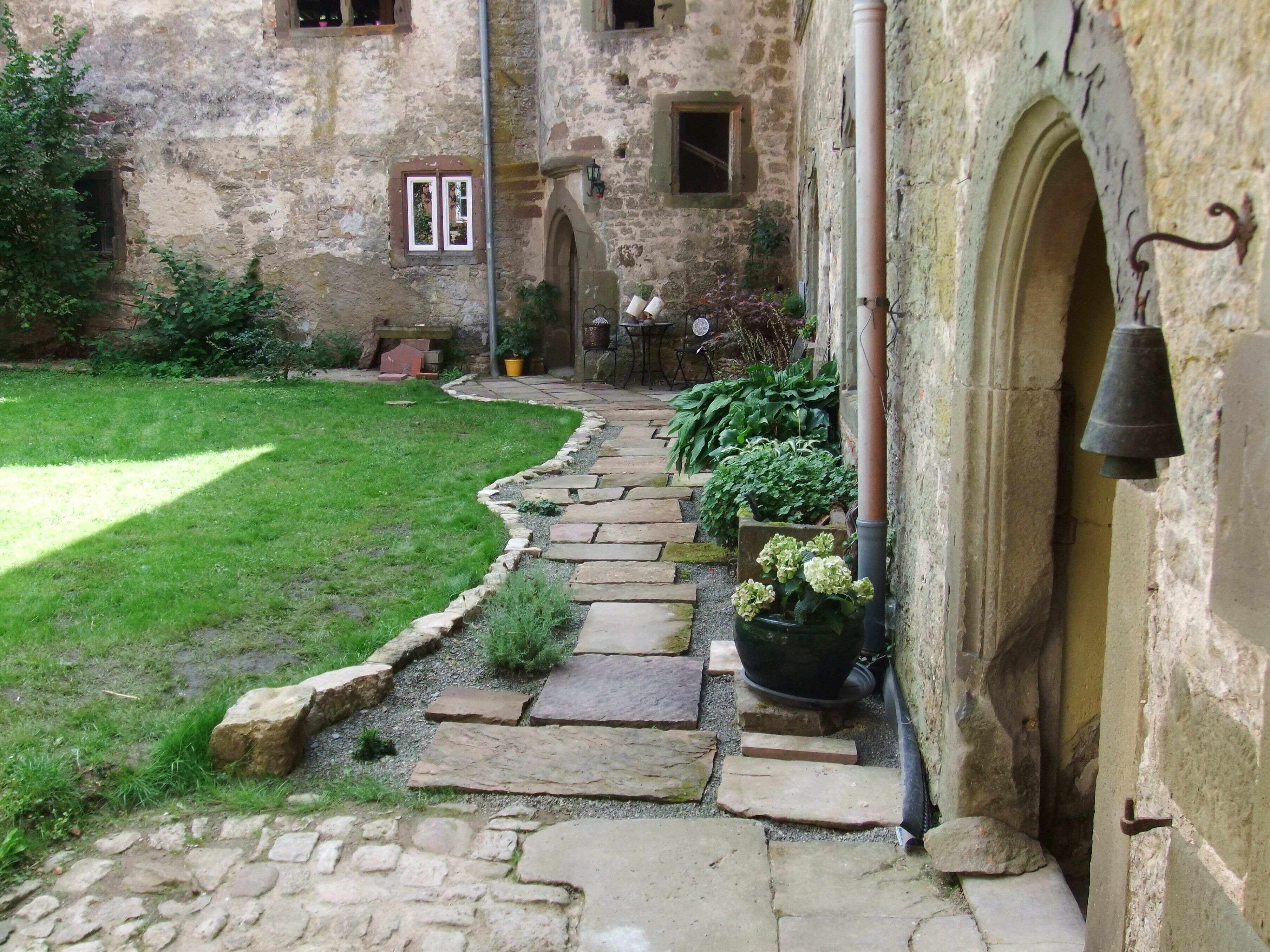 A stone pathway leading to a building with an arched entrance and a bell.