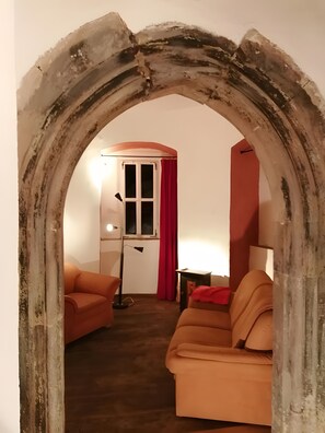 A room with a rustic archway, a red curtain, a white wall, and a brown floor.