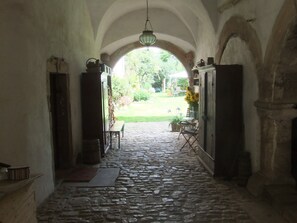 A stone-paved corridor with an arched ceiling, leading to an outdoor garden area.