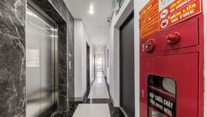 Un pasillo con suelo de mármol, un carretel de manguera contra incendios rojo y una señal de salida visible.