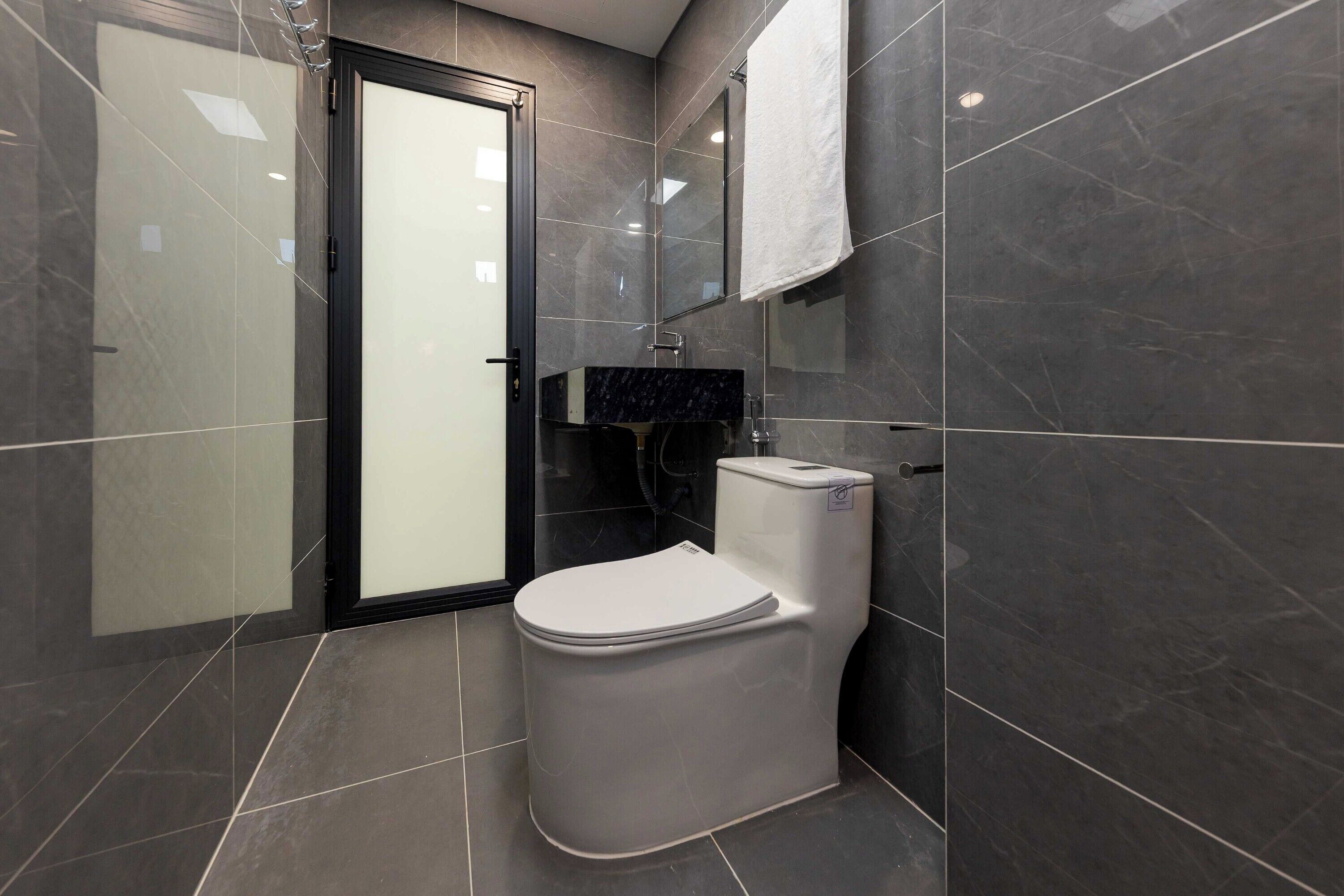A modern bathroom with a toilet, a glass shower enclosure, and a dark tiled floor.
