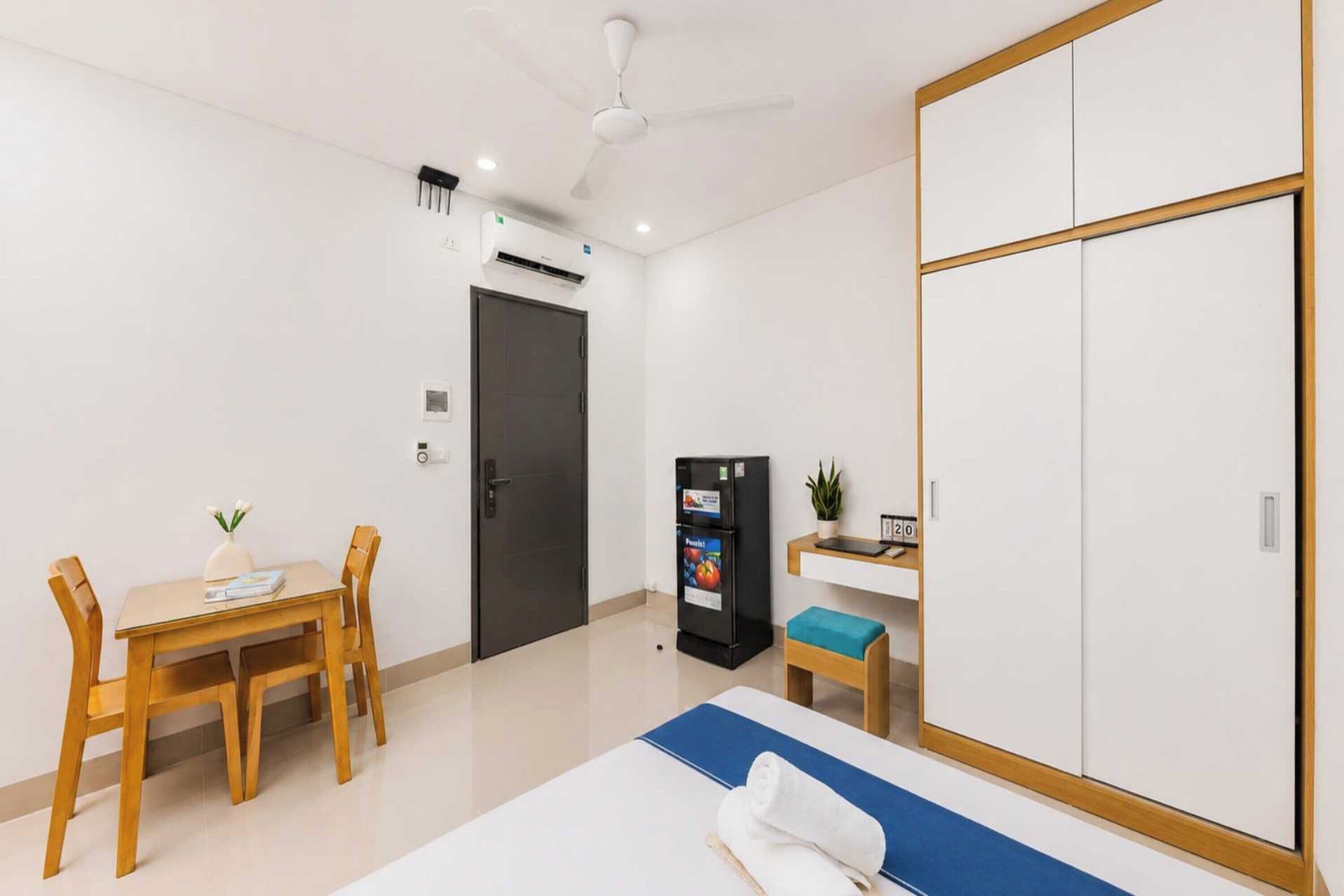 Une chambre d’hôtel comprenant un lit, un bureau, une armoire, une chaise, une petite table avec une plante et un appareil de climatisation.