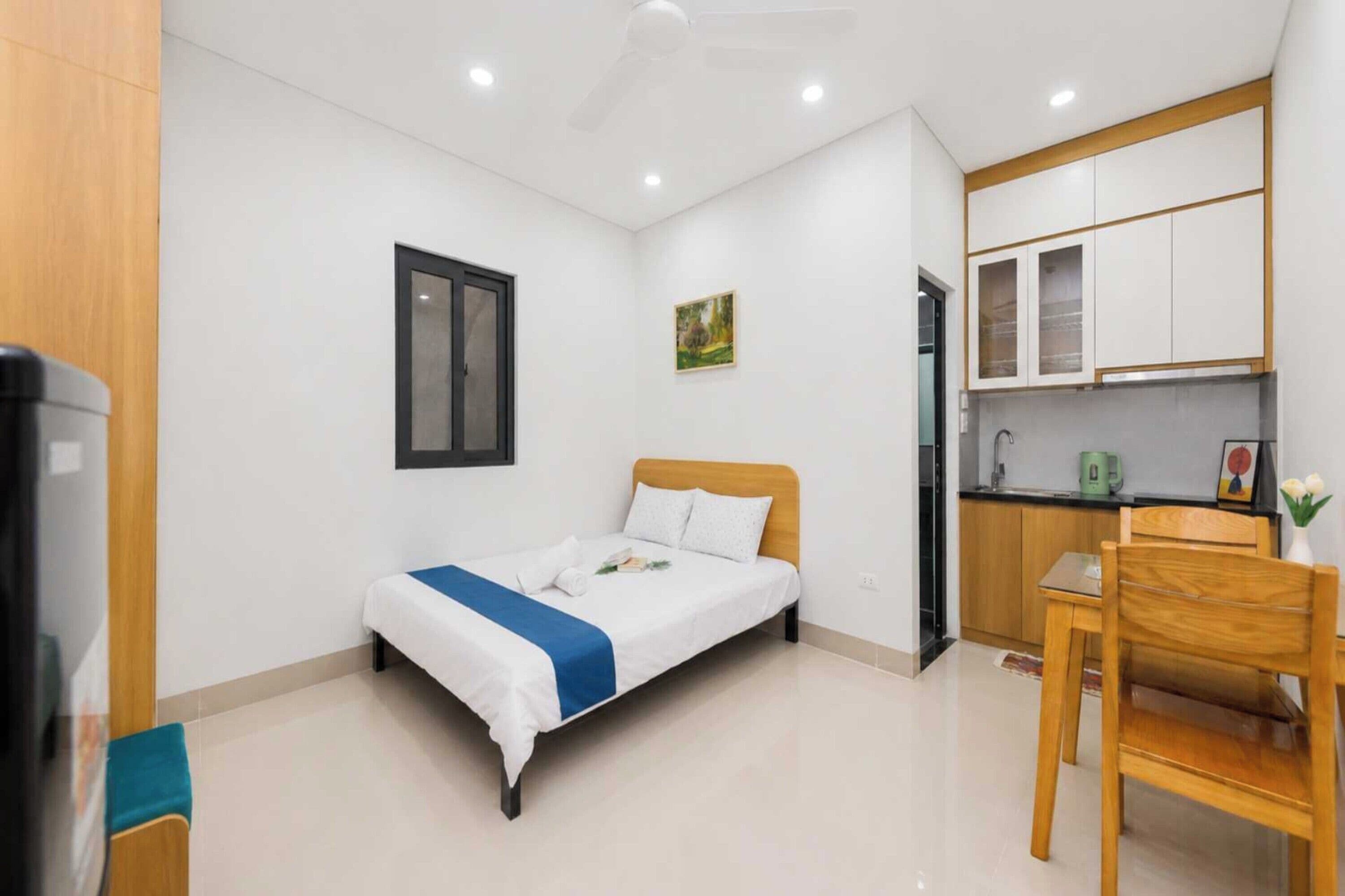 A compact hotel room with a single bed, a small kitchenette, and a wooden chair.