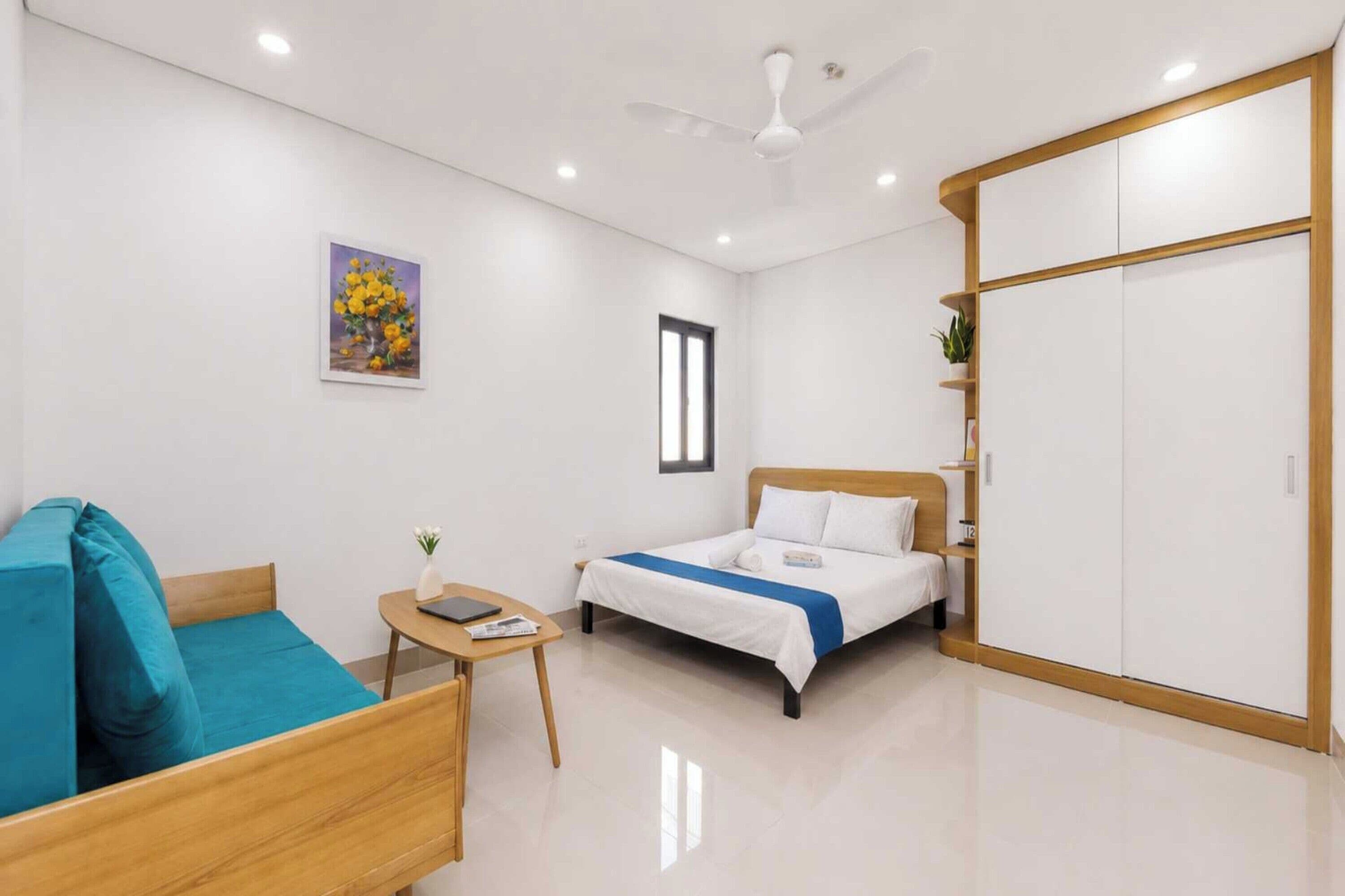 A modern bedroom with a bed, a sofa, a small table, a wardrobe, and a ceiling fan.