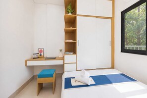 Un dormitorio con cama, escritorio, silla, armario y ventana.