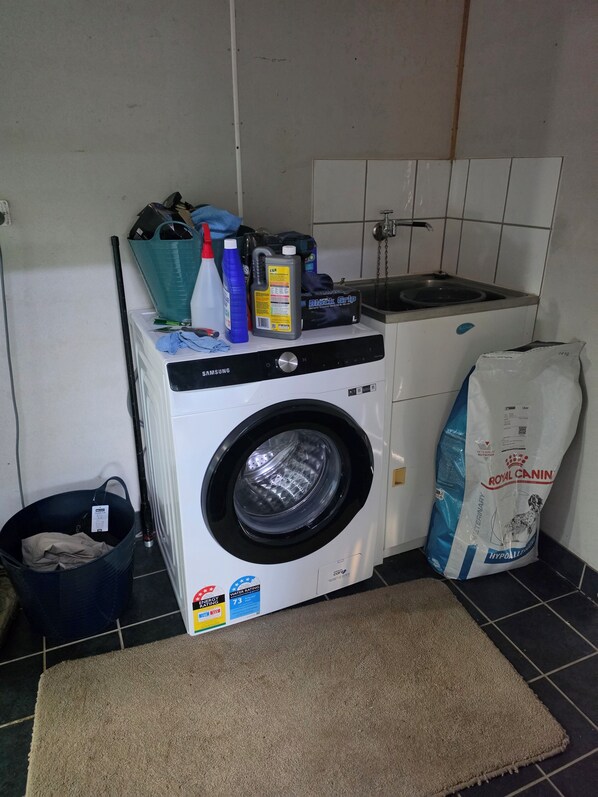 A compact laundry area with a front-loading washing machine, a small sink, and a bag of pet food.