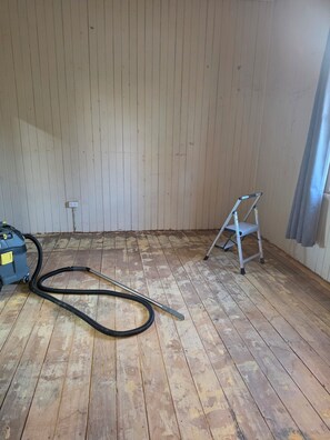 A room with a wooden floor, a power outlet, a vacuum cleaner, and a step ladder.