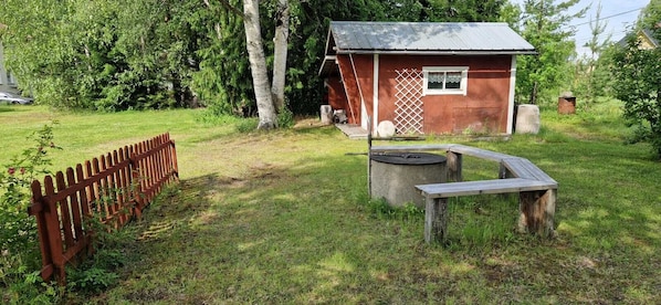 A rustic cabin with a metal roof, surrounded by a wooden fence and a concrete well.
