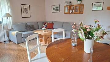 Un saló amb un sofà gris, una taula de centre de fusta, cadires blanques, un vas amb flors i armaris penjats a la paret.