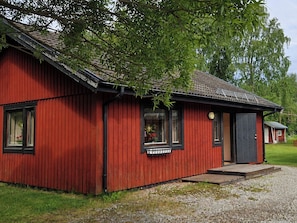 A red wooden house with a sloped roof, a small porch, and a window with a flower box.
