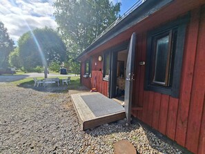 A red building with a wooden deck and a door open to a room.
